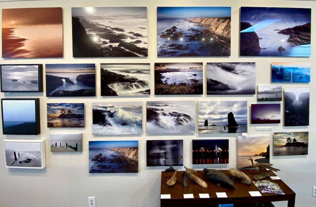 Photograph of Jonathan Pazer's main photography display wall, including his driftwood and metal sculptures and his poetry book as of April 2022 at the Mendocino Coast Photographers Gallery, Fort Bragg, CA